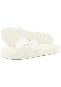 White slide sandals with four cross straps made of smooth material, a textured sole, and a small gold logo detail on the strap.