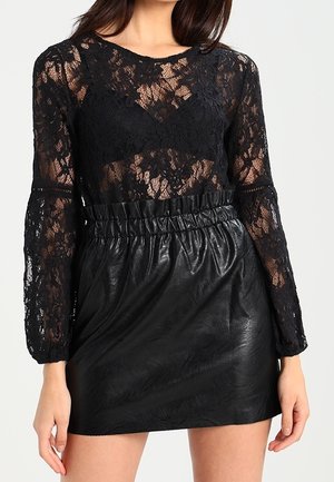 Černý dlouhý top z krajky s kulatým výstřihem, spojený s černou vysokým pasem umělou koženou sukní. Strukturované detaily a nařasený pas.