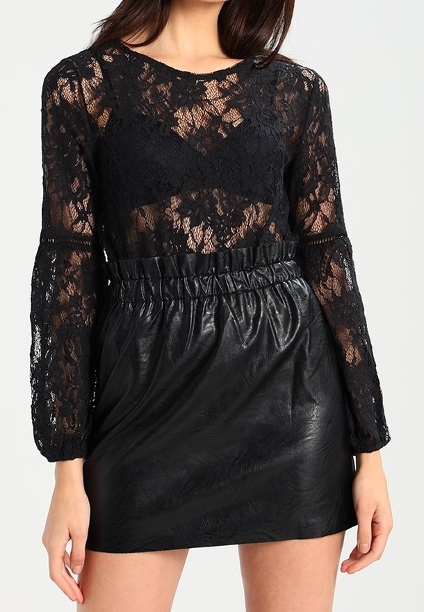 Haut à manches longues en dentelle noire avec un col rond, associé à une jupe taille haute en simili cuir noir. Détails texturés et taille froncée.
