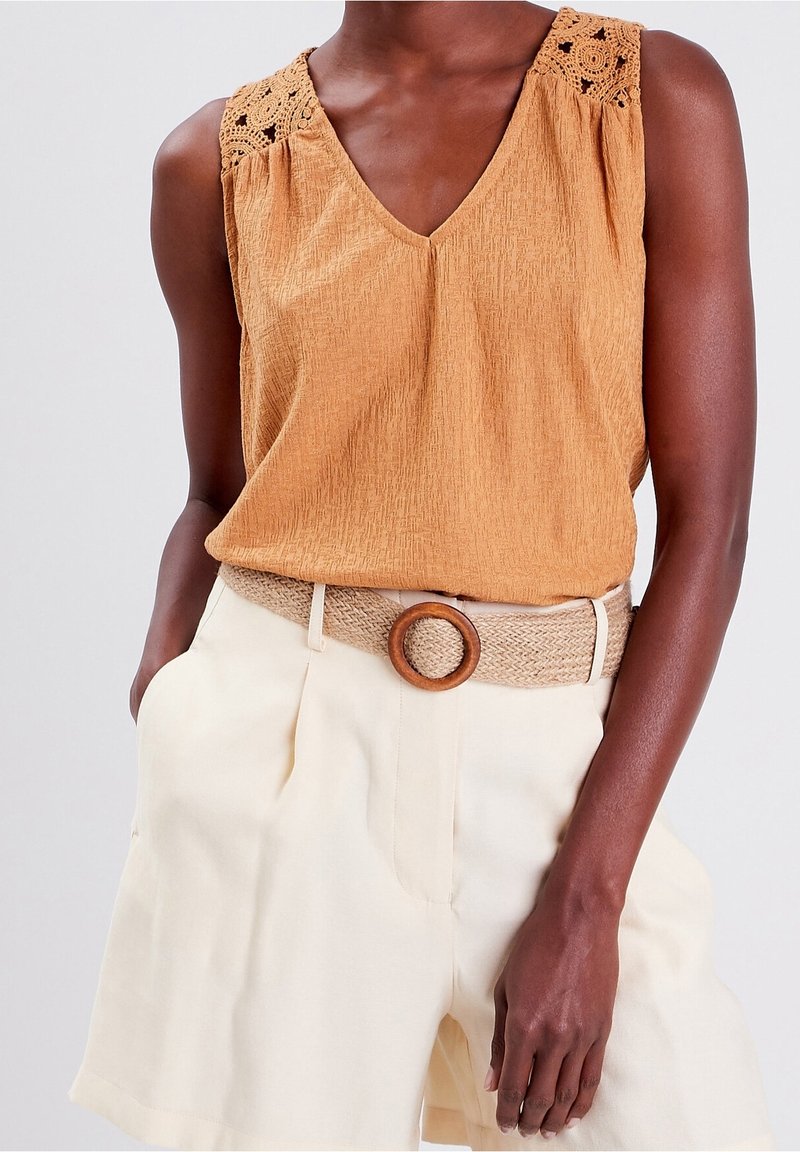 Haut sans manches de couleur moutarde avec un tissu texturé et des accents de dentelle aux épaules, associé à un short crème et une ceinture tissée avec une boucle ronde.