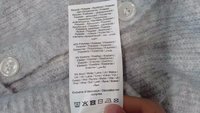 Țesătură gri deschis cu o textură moale și un nasture din plastic alb. Eticheta de îngrijire listează materialele: 40% poliester, 5% elastan, 5% lână.