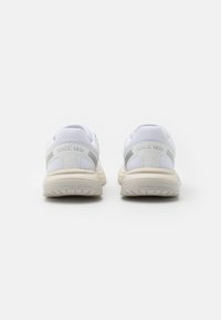 Weiße Sportschuhe mit einem Obermaterial aus Mesh, grauen Akzenten und dicken Sohlen. Auf der Ferse steht der eingeprägte Text "SEIT 1936". Sauberes Design.