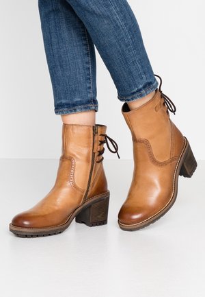 Braune Leder-Ankle-Boots mit einem klobigen Absatz, seitlichem Reißverschluss, dekorativer Schnürung und einem kontrastierenden weißen Stich entlang der Sohle.