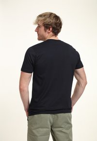 Black short-sleeve t-shirt with a crew neckline, made from soft fabric, paired with light green casual trousers. Simple design, no patterns.