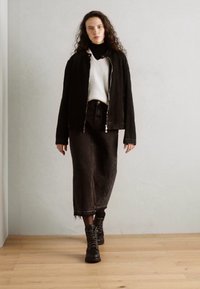 Veste en denim noire, pulls blanc, jupe en denim noire taille haute, bottes noires à lacets, avec une coupe décontractée et un ourlet effiloché.
