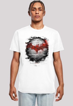 White cotton t-shirt featuring a distressed red and black bat symbol on a brick wall graphic. Short sleeves, crew neck, casual fit.