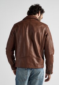 Brun läderjacka med en slät textur, med klassisk krage, synliga sömmar och dragkedjor vid ärmsluten. Bakifrån visar den en väldefinierad passform.
