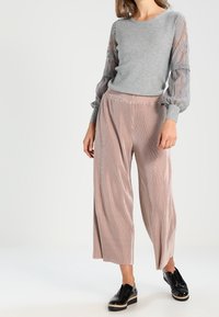 Pull gris avec manches bouffantes transparentes et broderie florale, associé à un pantalon rose plissé à jambes larges et des chaussures à plateforme noires.