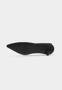 Chaussure plate noire à bout pointu vue du côté de la semelle, mettant en avant la semelle lisse et plate et le talon bas.
