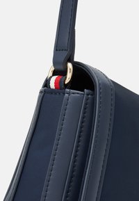 Bolso de mano azul marino con una forma estructurada, cuero suave, herrajes dorados y un acento de tela a rayas en rojo, blanco y azul.