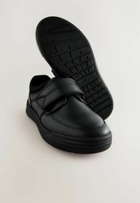 Chaussures noires avec une tige en cuir lisse, fermeture Velcro et semelle en caoutchouc texturé. Présente un bout arrondi et des détails de couture renforcés.