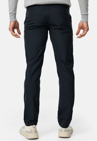 Pantaloni blu navy realizzati in un tessuto morbido, con design a gamba dritta, tasche posteriori e una comoda cintura, indossati con sneakers chiare.