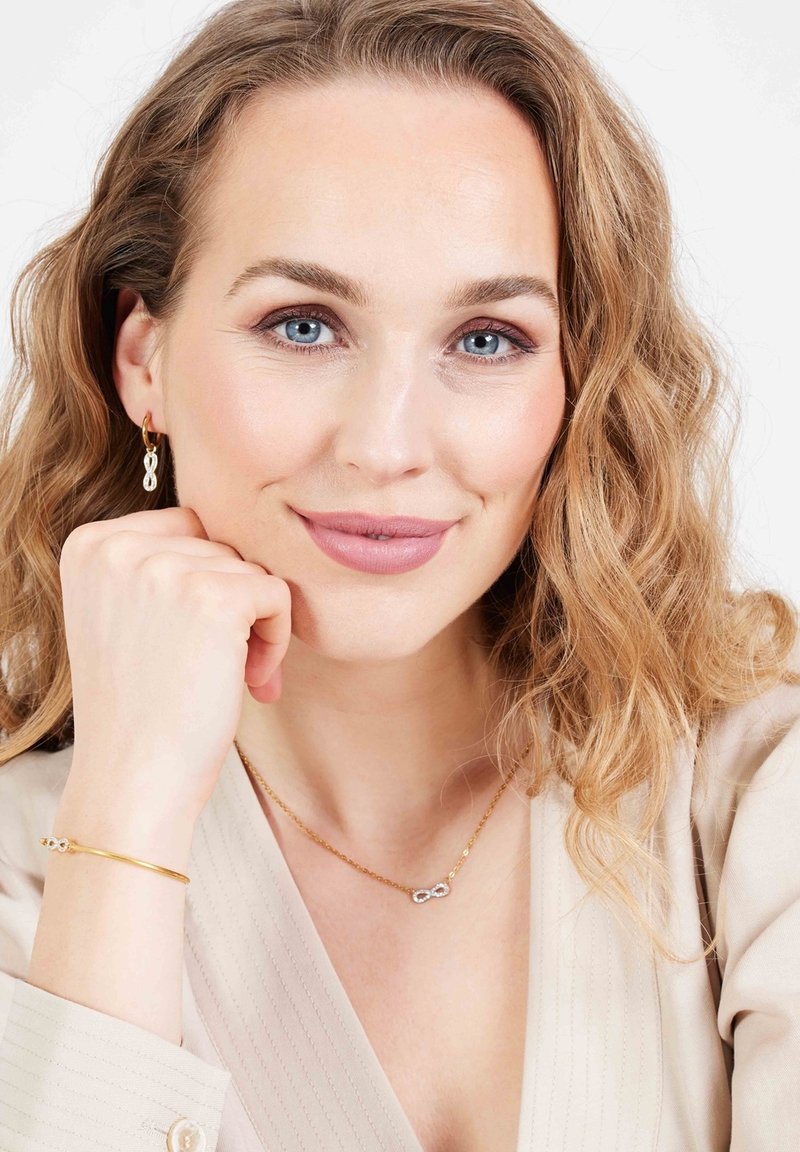 Gouden sieraden met een oneindigheid ontwerp, met een delicate kettinghalsketting en bijpassende oorbellen. Model heeft golvend, lichtbruin haar.