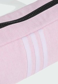 Sac en tissu rose avec une fermeture éclair noire, une surface texturée et un détail à trois rayures blanches.