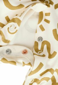 Cream-colored fabric featuring large gold abstract patterns, with metal snap fasteners in silver and rose gold along the edge.
