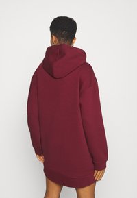Sudadera grande burdeos con una gran capucha, mangas largas y puños acanalados. Hecha de una tela suave, con un diseño sencillo.