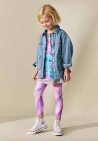 Kurtka jeansowa, koszulka z nadrukiem z grafiką z kreskówki, szara tunika i różowe legginsy z marmurkowym wzorem. Białe sneakersy za kostkę z gwiazdkowymi akcentami.