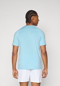 Lyseblå kortærmet træningsskjorte med raglanærmer og en glat tekstur, parret med hvide shorts, set fra bageste side.