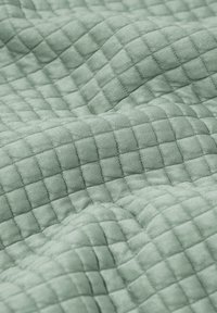 Strukturierter Stoff in sanftem Grün mit einem Rastermuster aus kleinen Quadraten, das eine fühlbare Oberfläche erzeugt. Glattes, leichtes Material.