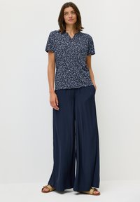 Marineblauwe blouse met bladerenpatroon, korte mouwen en een v-hals. Gecombineerd met losse, donkerblauwe broek en bruine sandaaltjes met bandjes.