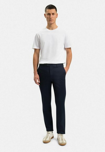 Vit kortärmad t-shirt i kombination med marinblå skräddarsydda byxor och beige sneakers. Slät tygkvalitet, minimalistisk design, figursydd siluett.