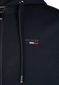 Navy Zip-Hoodie aus strukturiertem Stoff. Mit einem gebrandeten "HECHTER"-Logo und einem dreifarbigen Akzent in Rot, Weiß und Blau neben dem Logo.