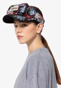 Black cap with a wide brim and a colorful, graphic band. Features zippered pouch on top with brand logo. Textured fabric with tropical patterns.