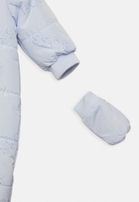 Přechodová světle modrá bunda s vyraženým logem značky, žebrovanými manžetami a sladěnou odnímatelnou rukavicí. Hladká, lesklá textura látky.