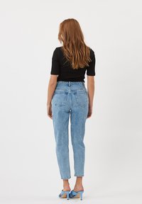 Jeans azzurri a vita alta con vestibilità rilassata, dotati di tasche posteriori e orlo risvoltato, abbinati a un top nero aderente e tacchi blu.
