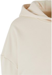 Haut à capuche couleur crème avec une texture douce, doté d'une grande capuche, de manches tombantes et d'un design décontracté.