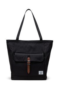Sac fourre-tout en toile noire avec une poche avant, une sangle en cuir à boucle et deux poignées pour l'épaule. Présente une étiquette de marque en bas à droite.