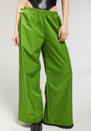 Pantaloni larghi verdi realizzati in un materiale lucido e leggero. Presentano una vita con cordino elastico e tasche laterali.