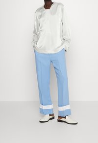 Silky white long-sleeve top with a hood, paired with light blue trousers featuring white cuffs and white slip-on shoes. Elegant, relaxed fit.