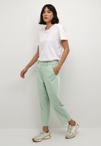 Pantalons tapered vert menthe avec poches latérales, associés à un t-shirt blanc uni et des sneakers beige clair. Finition en tissu lisse, lignes épurées.