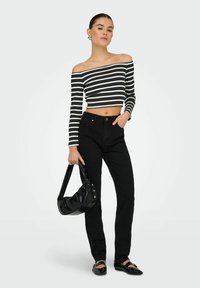 Sorte højtaljede jeans parret med en sort og hvidstribet cropped off-the-shoulder top. Holder en sort taske med sølvdetaljer.