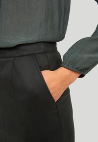 Černé kalhoty s texturovaným povrchem, které mají boční kapsy a přiléhavý pás. Doprovodný top je zelený, s nařasenými rukávy.