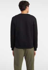 Black sweatshirt with a crew neckline and ribbed cuffs, shown from the back, paired with olive green pants. Soft, textured fabric.
