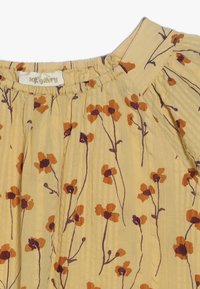 Jasnożółta tkanina z rdzawopomarańczowym i ciemnobrązowym wzorem kwiatowym, zebrany dekolt i miękki, teksturowany materiał.