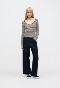 Csíkos hosszú ujjú felső kerek nyakkivágással, széles szárú sötét farmernadrággal párosítva. A modell fekete-fehér cipőt visel.