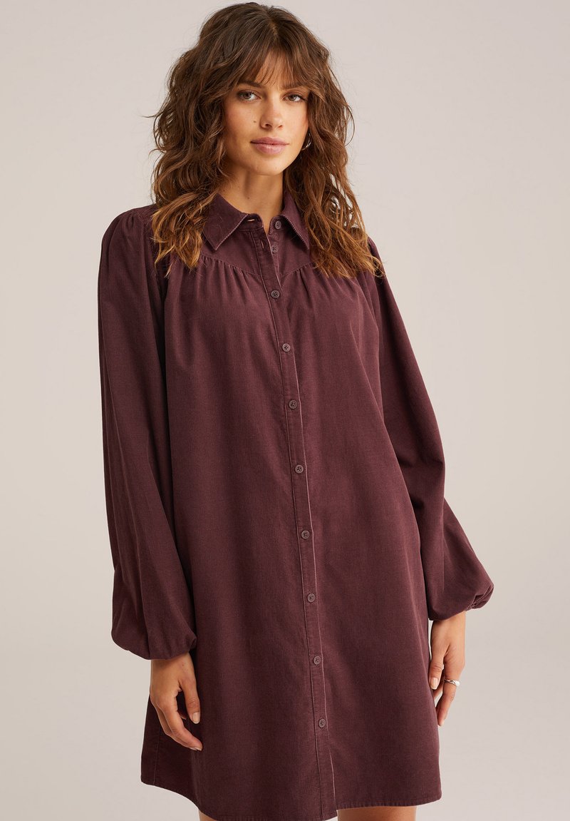 Abito camicia lungo bordeaux con maniche lunghe, apertura con bottoni davanti, colletto classico, giromanica arricciato e maniche ampie e elastiche. Tessuto morbido e testurizzato.