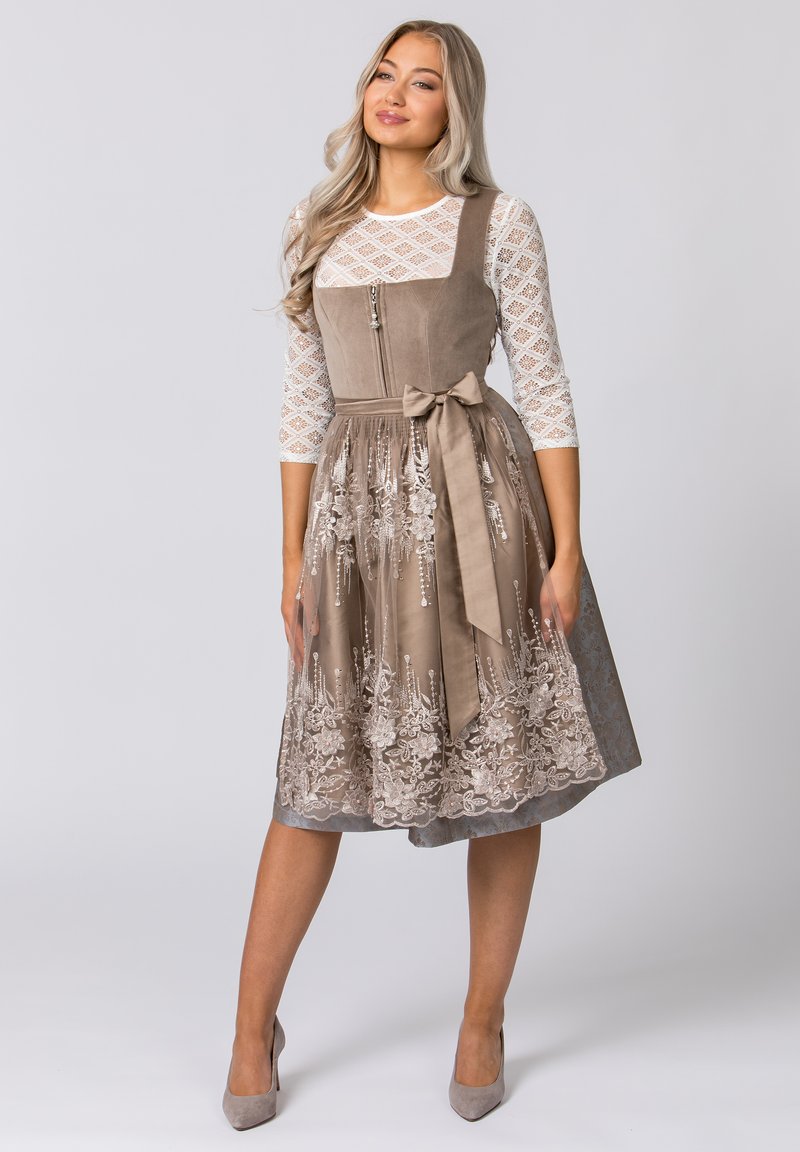 Brown suede dress with a fitted bodice, embroidered lace skirt, and a bow at the waist. Features a white lace long-sleeve top.