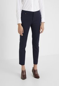 Granatowe, dopasowane spodnie o gładkim wykończeniu, wąskim kroju i subtelnym logo na pasku, zestawione z brązowymi butami na obcasie.