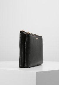 Sort læderpung med to lynlåslommer, tekstureret overflade og guldfarvede hardware-detaljer. Minimalistisk design, rektangulær form.