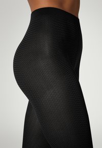 Leggings neri con texture a nido d'ape, dotati di una ampia vita nera. Il tessuto sembra elasticizzato e aderente.