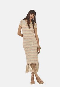 Vestido de punto en colores pastel, con un corte ajustado en la parte superior y un dobladillo con flecos. La modelo lleva sandalias de cuña beige con tiras y pulseras apiladas.