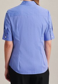 Ljusblå kortärmad blus med krage, som har en skräddarsydd passform, knapppynt på ärmarna och en mjuk tygtextur.