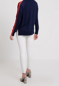 Námořnický svetr s červenými pruhy, doplněný bílými skinny džíny. K outfitu se skvěle hodí texturované lodičky s hadím vzorem.