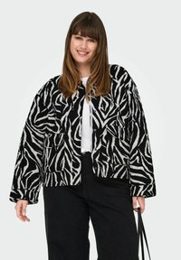 Gilimota su juodai balta zebro raštu, su mygtukų uždarymu ir dviem priekiniams kišenėms, derinama su balta marškinėliais ir juodomis kelnėmis.