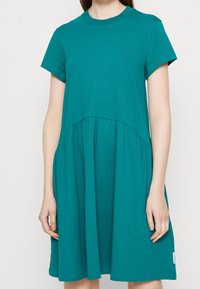Tyrkysové šaty s krátkým rukávem vyrobené z jemné bavlny, s nařasenou sukní, která se rozprostírá pod pasem, s kulatým výstřihem a bez viditelných vzorů.
