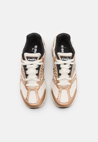 Witte en metallic gouden sportschoenen met een bovenwerk van mesh, platte veters, gevoerde kraag en zwarte binnenvoering. Diadora-logo op de tong.